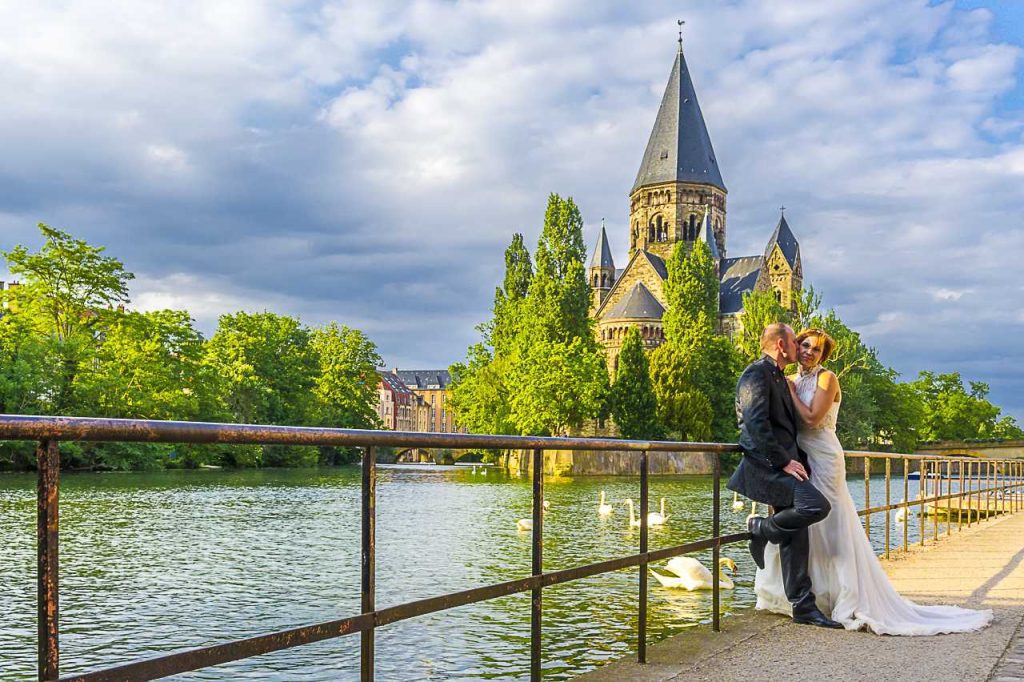 Thierry et Aurore Nadé, photographes de mariage, capturant un moment intime sur un pont avec un château et des cygnes en arrière-plan.