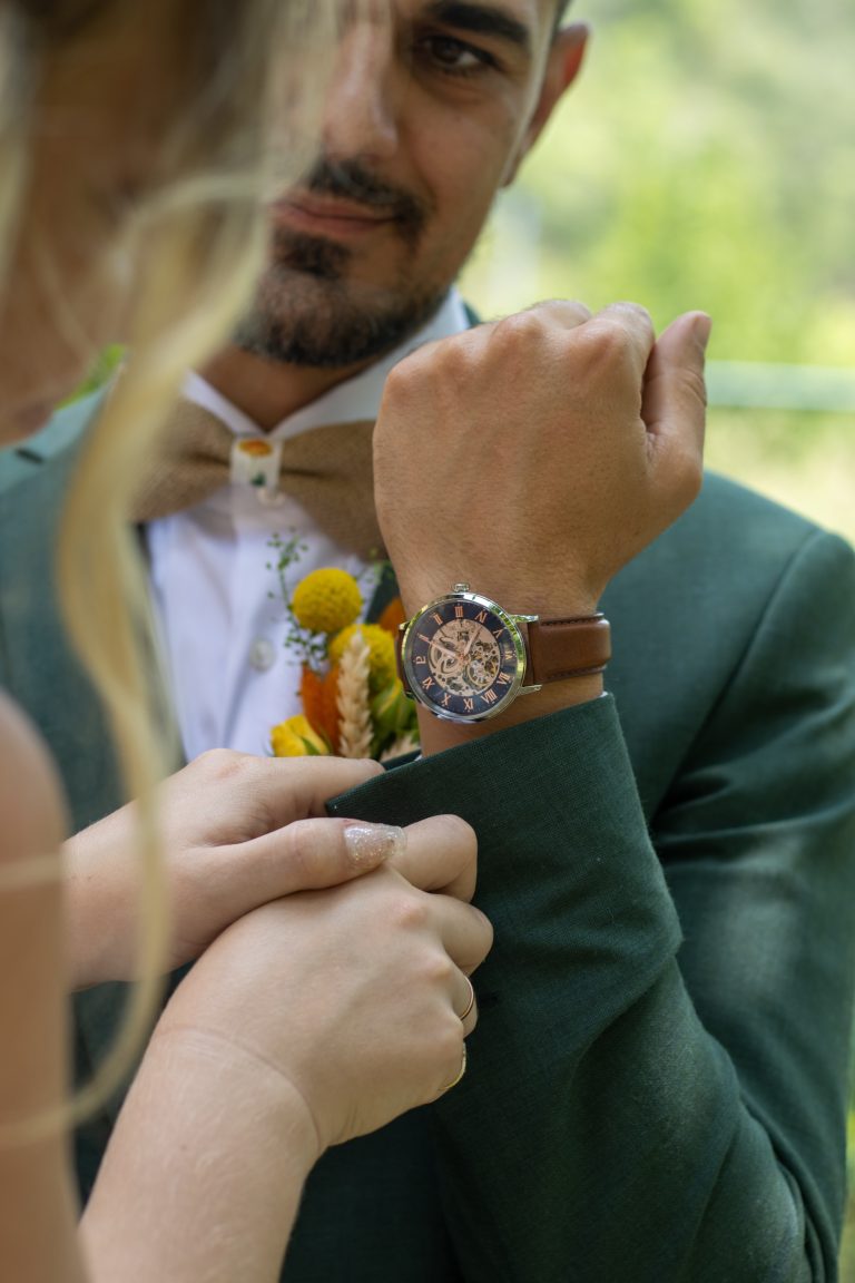 Couple de mariés se tenant la main, elle avec une bague et des ongles pailletés, lui avec une montre élégante