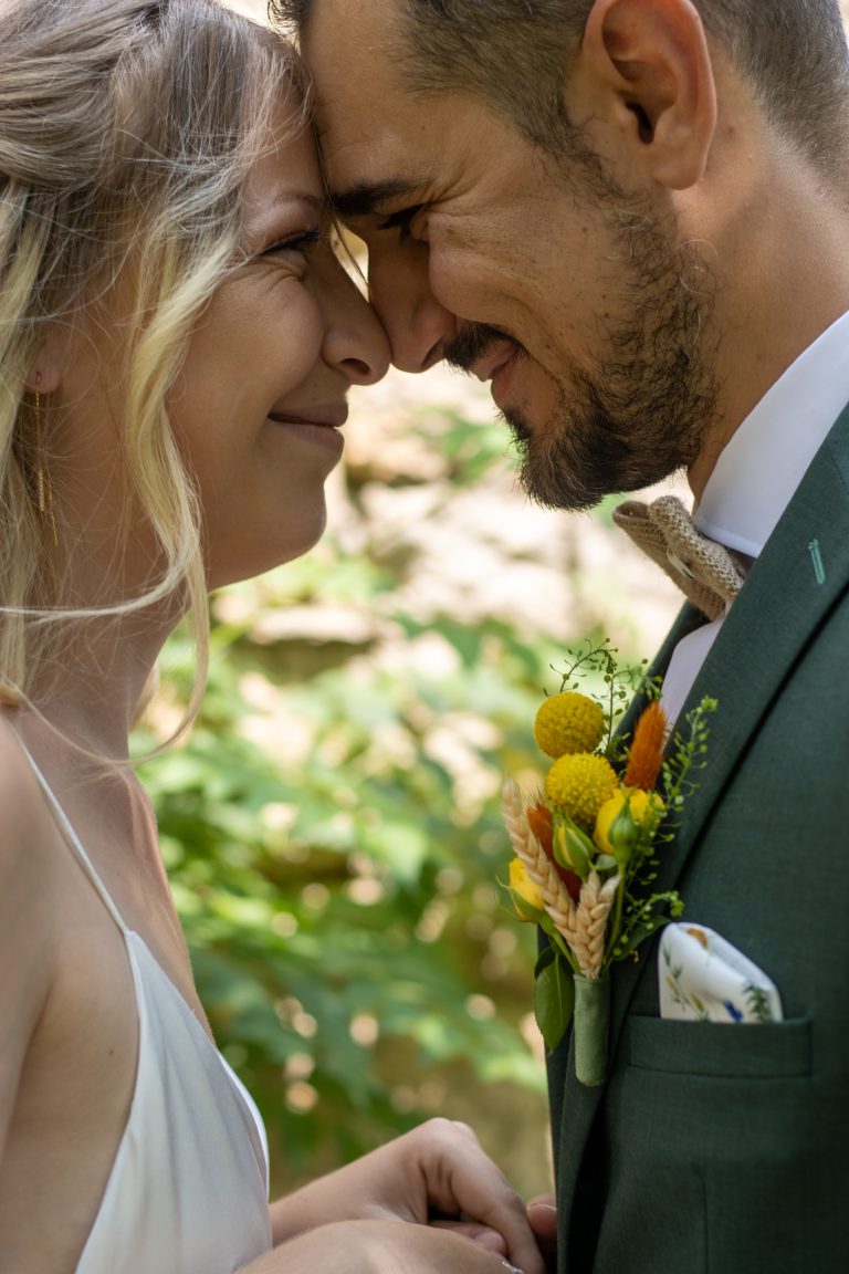 Mariés souriants échangeant un regard complice sous leurs couronnes de fleurs