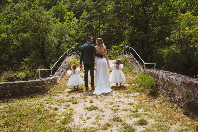Couple de mariés tenant la main de deux enfants sur un pont, dos à l'appareil.