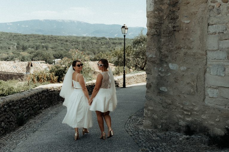 Deux mariées de dos, marchant main dans la main sur un chemin pavé.