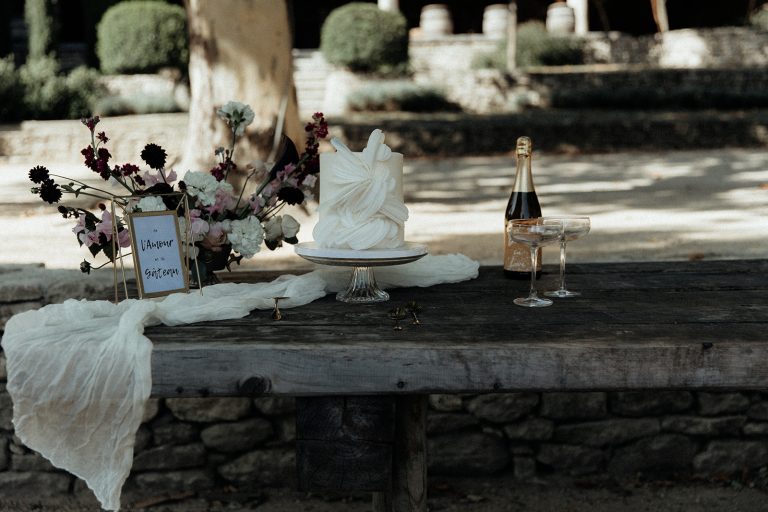Gâteau de mariage artistique avec champagne et bouquet sur une table rustique.