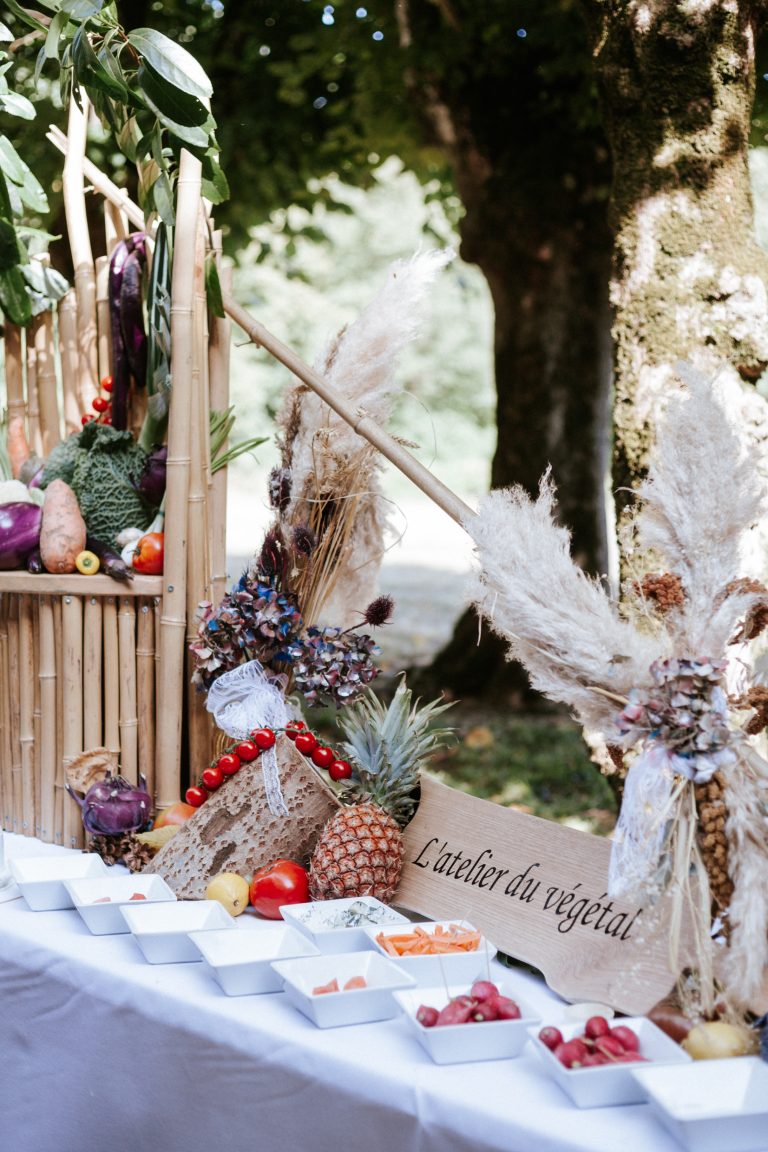 Stand traiteur décoré en extérieur avec fruits, légumes frais et fleurs séchées, portant l’enseigne « L’atelier du végétal »