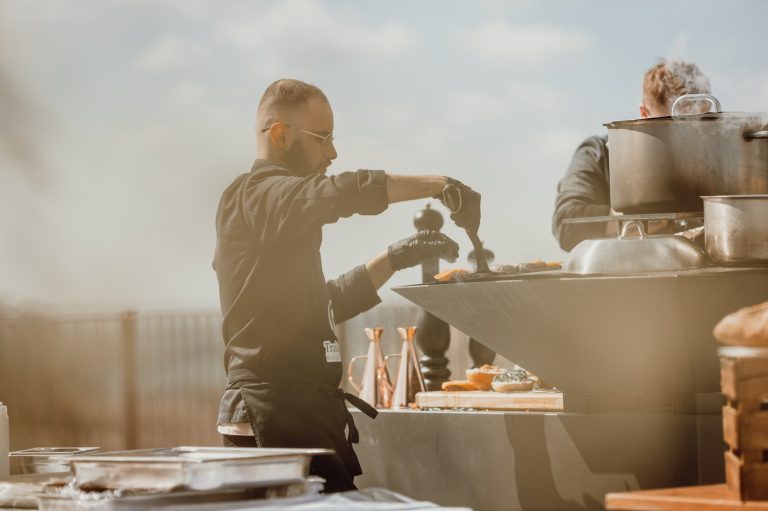 Un chef cuisinier prépare un plat au brasero en plein air lors d’un mariage.
