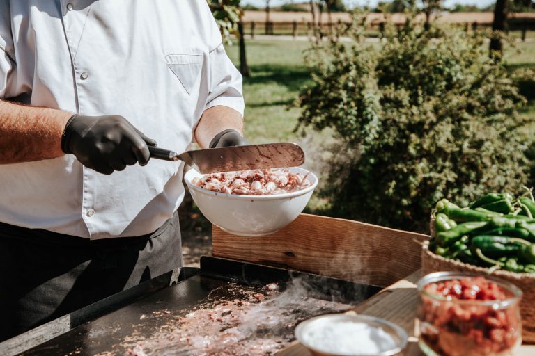Chef en extérieur versant des encornets frais dans une poêle chaude, avec des légumes disposés à côté.