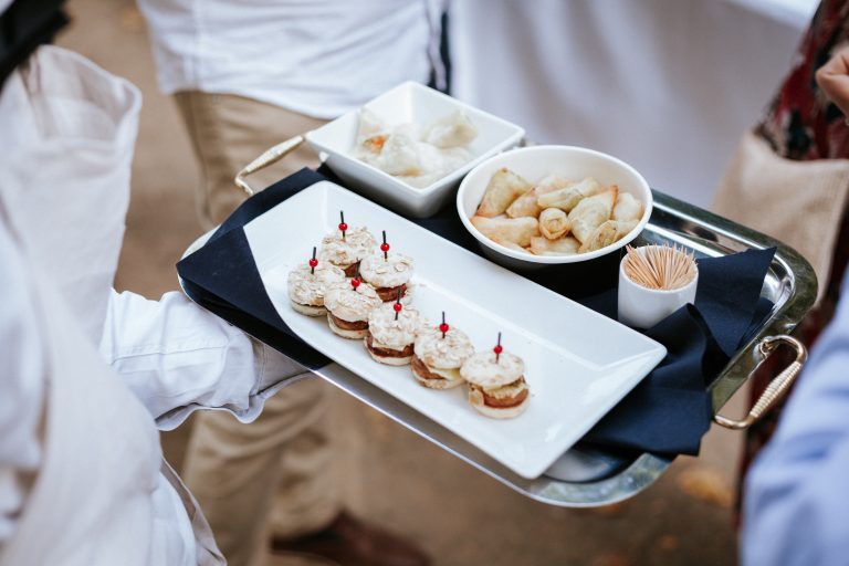 Plateau de bouchées salées avec mini-burgers et petits nems, servis sur plateau argenté avec pics apéritifs.