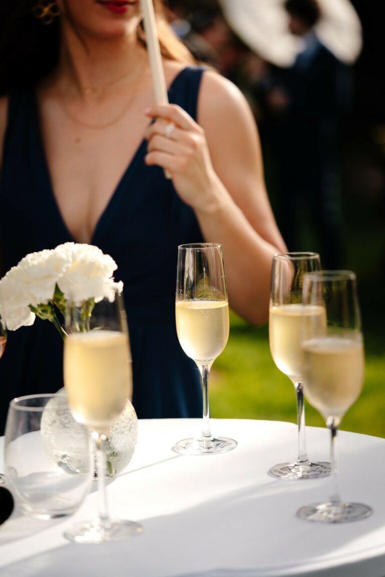 Flûtes de champagne posées sur une table nappée de blanc, avec une invitée en robe bleu marine tenant un éventail.