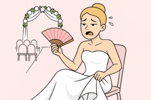 Une mariée assise en robe blanche, visiblement accablée par la chaleur, s'évente avec un éventail rose pendant son mariage d'été en extérieur.