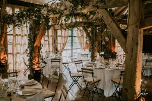Salle de réception de mariage décorée dans un esprit champêtre chic avec poutres en bois, feuillages et tables dressées.