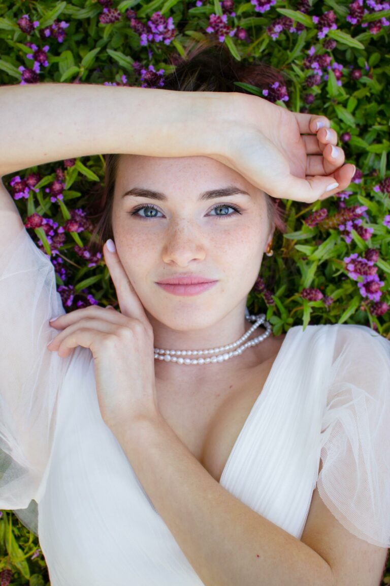 Camille, fondatrice de Denesis, allongée dans l’herbe, portant un collier de perles.