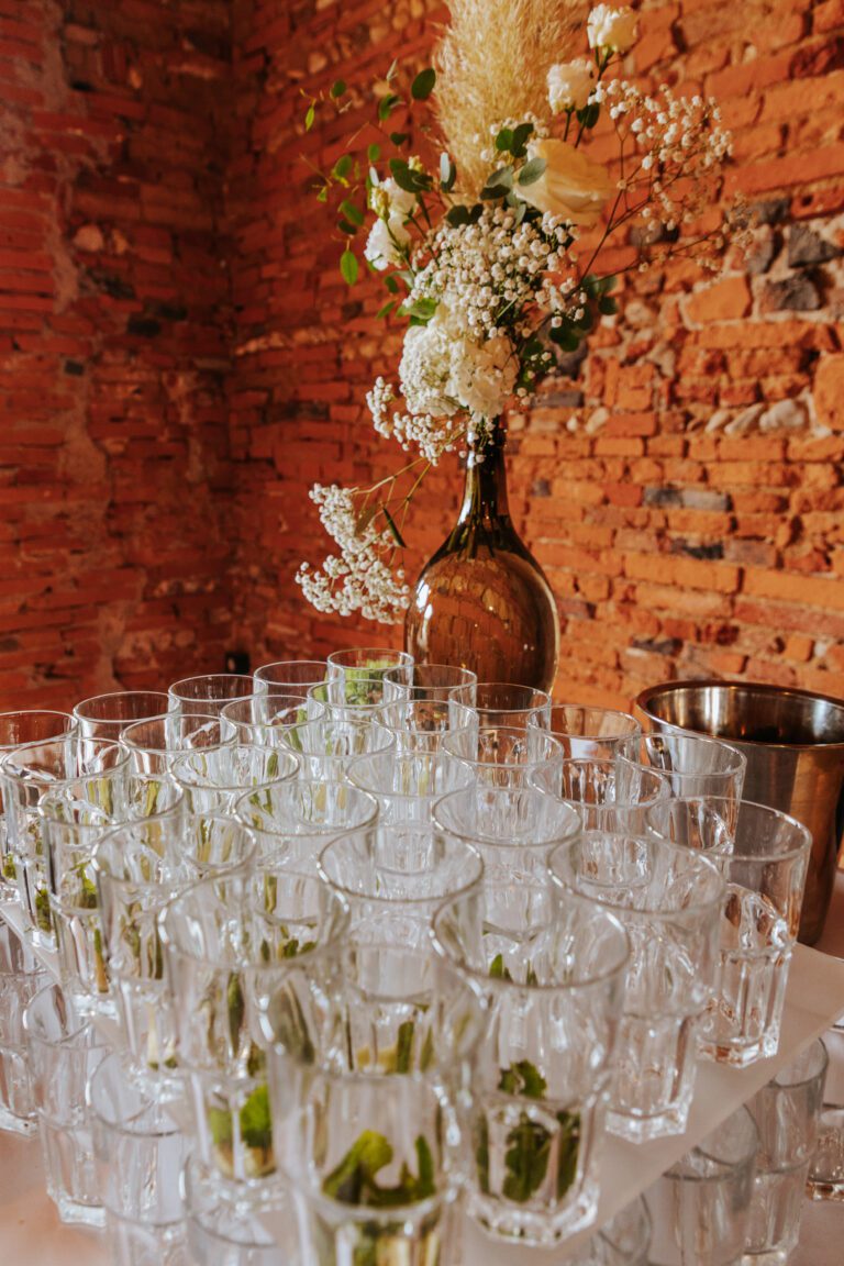 Verres à mojito prêts à l’emploi sur une table de réception, avec un grand bouquet de fleurs blanches et séchées en arrière-plan.