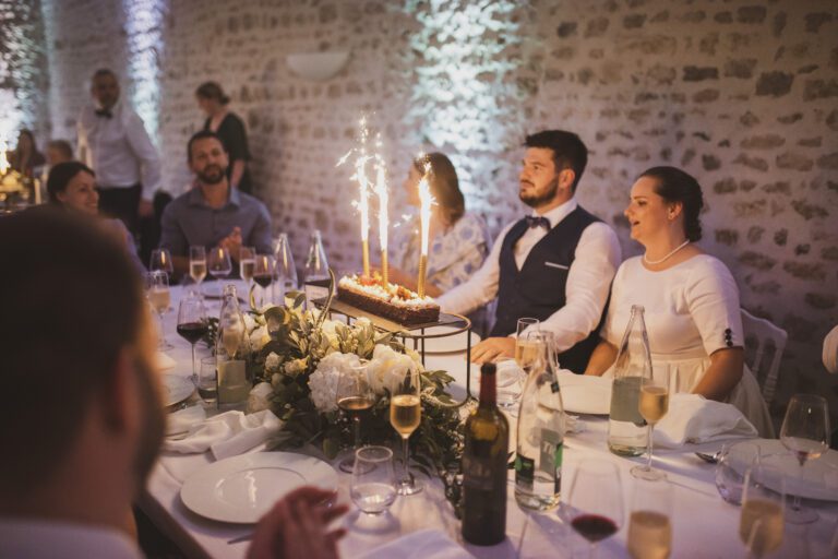 Gâteau de mariage en forme de bûche avec cierges magiques, entouré d’invités souriants lors de la soirée.