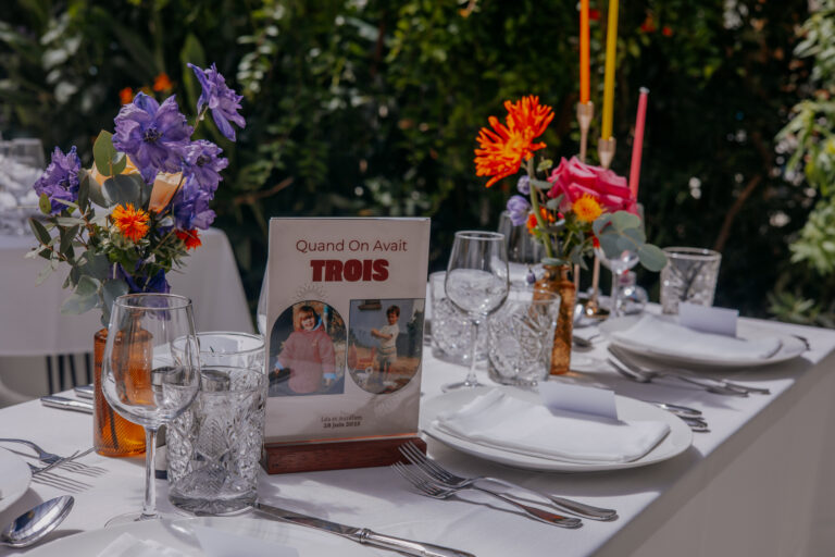 Table de mariage décorée avec des fleurs colorées, un menu personnalisé avec photos d’enfance, chandeliers colorés et vaisselle élégante.
