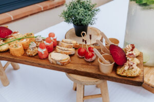 Planche en bois garnie de bouchées apéritives raffinées et colorées : foie gras, billes de pastèque, roulés salés, mini brochettes, verrines et madeleines salées.