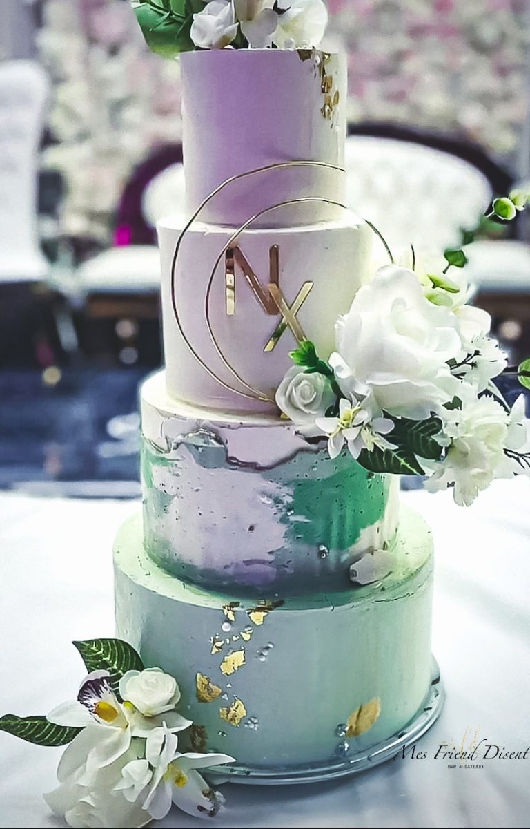 Wedding cake à quatre étages pastel décoré de fleurs blanches, feuilles dorées et cercles dorés personnalisés avec des initiales.